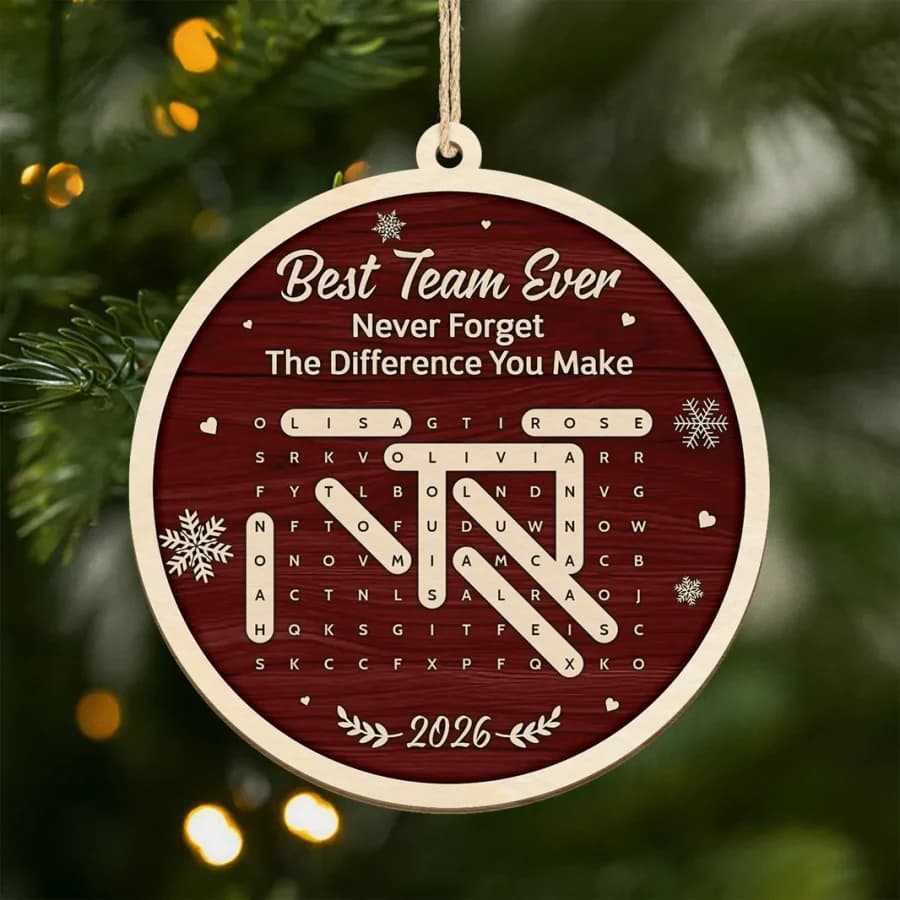 A round wooden ornament hanging on a Christmas tree, a letter grid with several names traced out and the words Best Team Ever above it